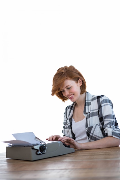 femme hipster souriante assise à un bureau, tapant sur sa machine à écrire