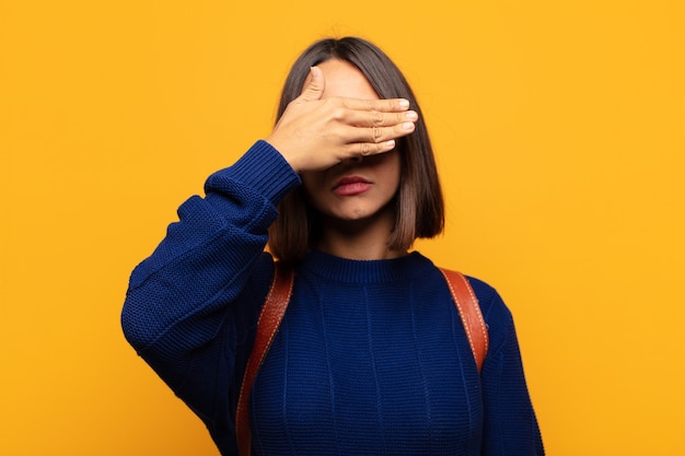 Femme hispanique couvrant les yeux d'une main se sentant effrayée ou anxieuse, se demandant ou attendant aveuglément une surprise