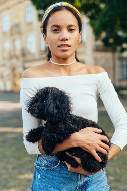 femme hispanique debout avec un chien mignon dans ses bras sur fond d'une belle vue urbaine