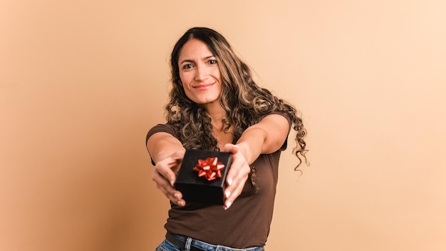 Une femme hispanique donne un cadeau en regardant la caméra.