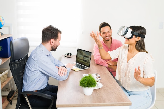 Femme hispanique excitée avec des lunettes de réalité virtuelle regardant un voyage de leurs vacances à l'agence de voyage avec son mari