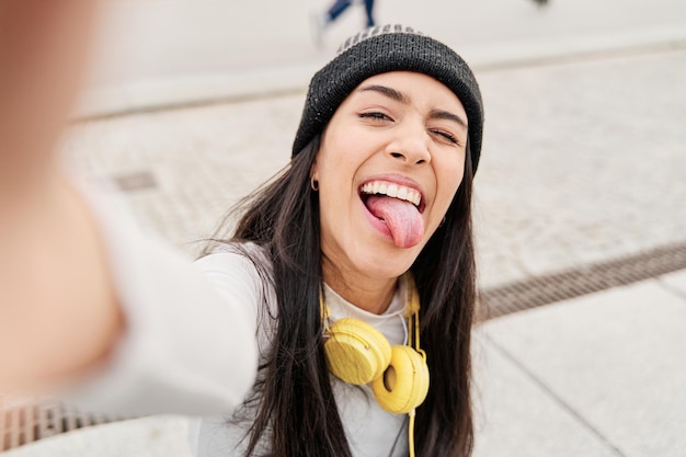 Femme hispanique faisant une drôle de tête tout en prenant un selfie qui sort sa langue et un clin d'œil