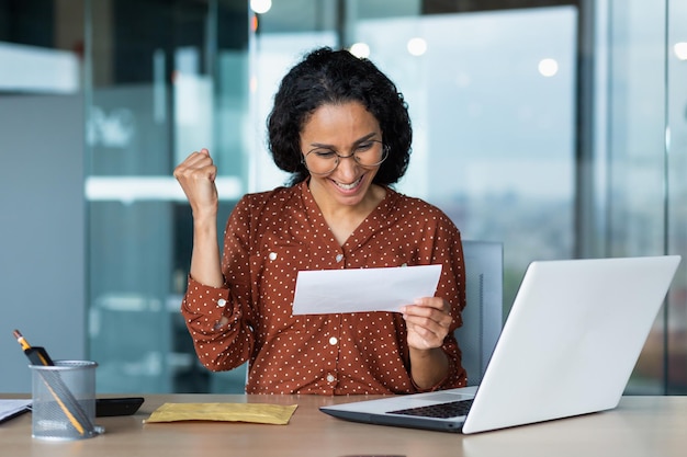 Une femme hispanique a reçu une lettre heureuse de la femme d'affaires de la banque lit et se réjouit de célébrer