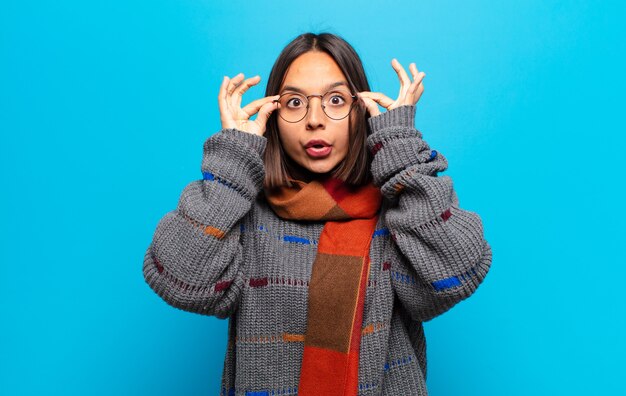 Femme hispanique se sentant choquée, étonnée et surprise, tenant des lunettes avec un regard étonné et incrédule