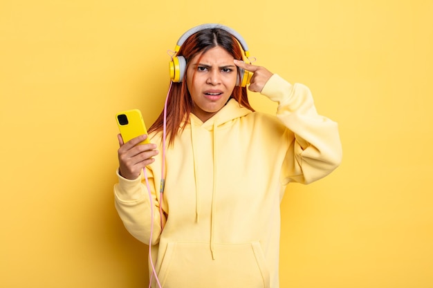 Femme hispanique se sentant confuse et perplexe montrant que vous êtes un casque fou et un concept de smartphone