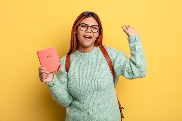 Femme hispanique souriant joyeusement, agitant la main, vous accueillant et vous saluant. concept étudiant et calendrier