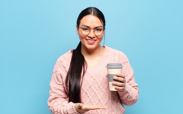 Femme hispanique souriant joyeusement, se sentant heureuse et montrant un concept dans l'espace de copie avec la paume de la main