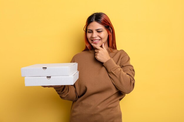 Photo femme hispanique souriante avec une expression heureuse et confiante avec la main sur le menton. concept de pizzas à emporter