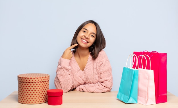 Femme hispanique souriante pointant avec confiance vers son propre large sourire, positif, détendu