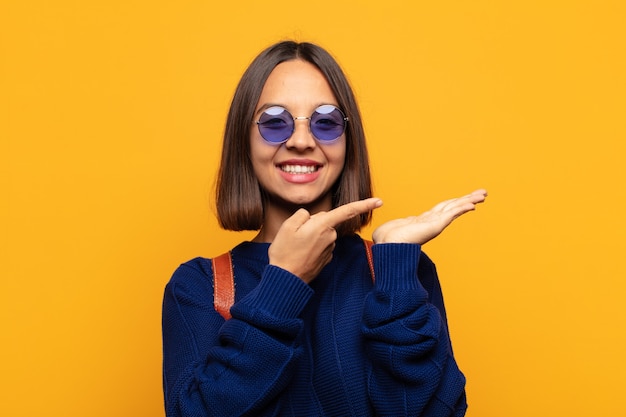 Femme hispanique souriante, se sentant heureuse, insouciante et satisfaite, pointant vers le concept ou l'idée sur l'espace de copie sur le côté