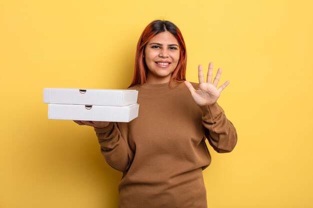 Femme hispanique souriante et semblant amicale, montrant le numéro cinq. concept de pizzas à emporter