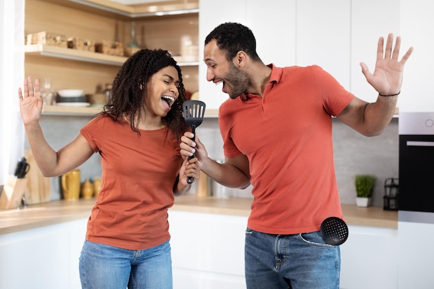 Une femme et un homme afro-américains du millénaire satisfaits s'amusent à danser ensemble et à écouter de la musique chanter au microphone imaginaire