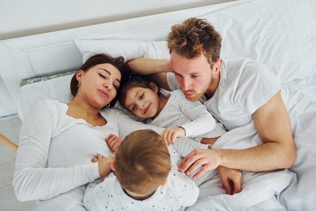 Femme et homme allongés sur le lit avec leurs enfants Intérieur et design d'une belle chambre moderne pendant la journée