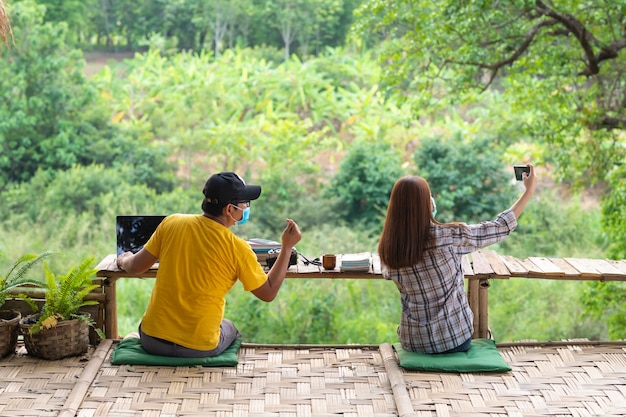 Femme et homme asiatique en distanciation sociale assis sur un banc et prendre un selfie au milieu de la nature, concept de distanciation sociale.