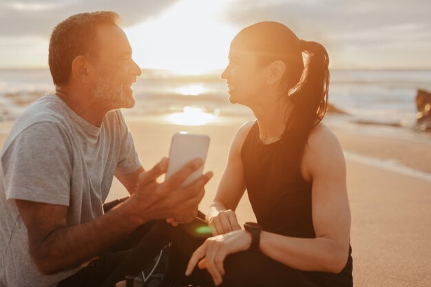 Une femme et un homme européens mûrs et satisfaits en vêtements de sport se reposent de l'entraînement avec un smartphone