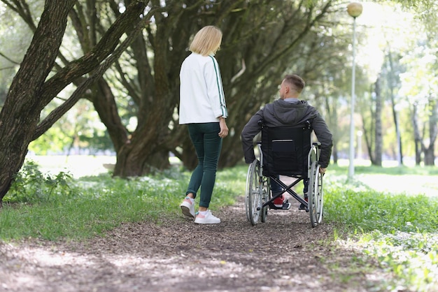 Une femme et un homme en fauteuil roulant marchent dans la réhabilitation du parc et un soutien amical pour