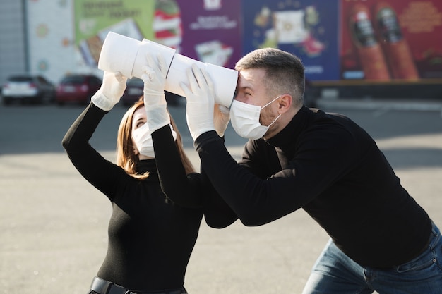 Une femme et un homme portant un masque anti-coronavirus tiennent de gros rouleaux de papier toilette