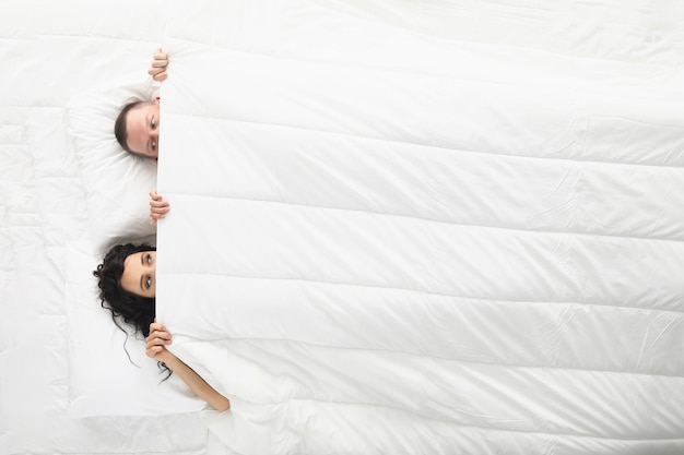 Photo femme et homme se regardant l'un l'autre sous une couverture blanche couple éveillé au lit