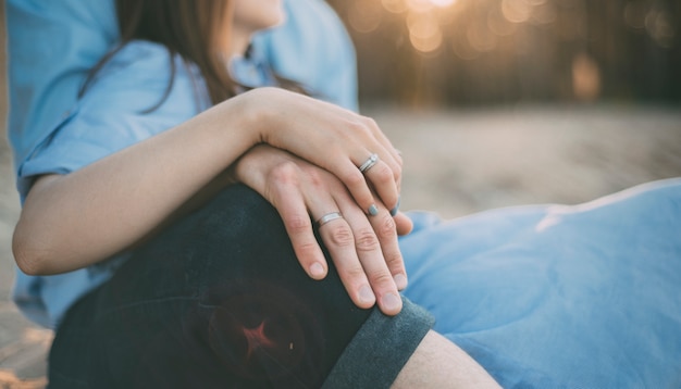 Femme et homme sont assis sur le sable avec les mains ensemble