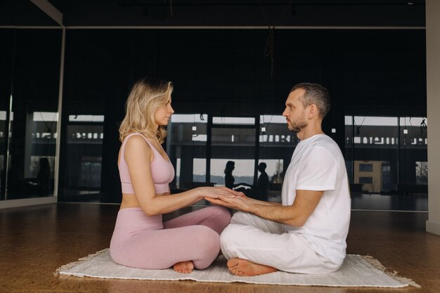 Une femme et un homme sont engagés dans une méditation en couple main dans la main dans la salle de gym