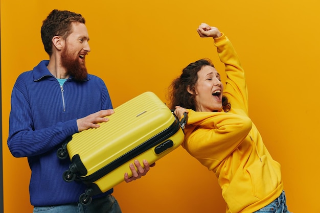 Photo femme et homme souriant valises à la main avec valise jaune et rouge souriant joyeusement et fond jaune tordu partant en voyage vacances en famille voyage jeunes mariés