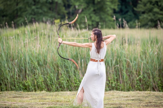 Une femme hongroise vêtue d'une robe en lin avec un arc se tient sur le terrain