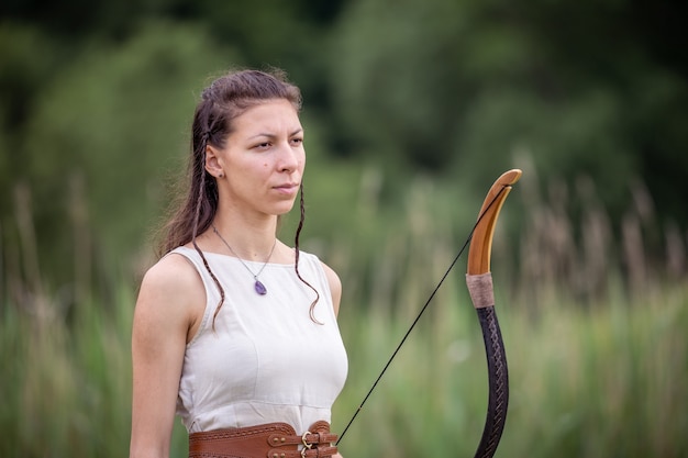 Une femme hongroise vêtue d'une robe en lin avec un arc se tient sur le terrain