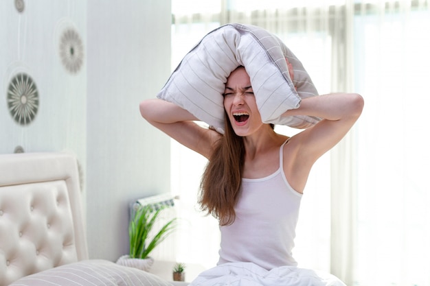 Femme Hurlante En Colère Souffrant Et Dérangée Par Des Voisins Bruyants Et Couvrant Ses Oreilles Avec Un Oreiller Tout En Essayant De Dormir Dans Son Lit à La Maison Tôt Le Matin