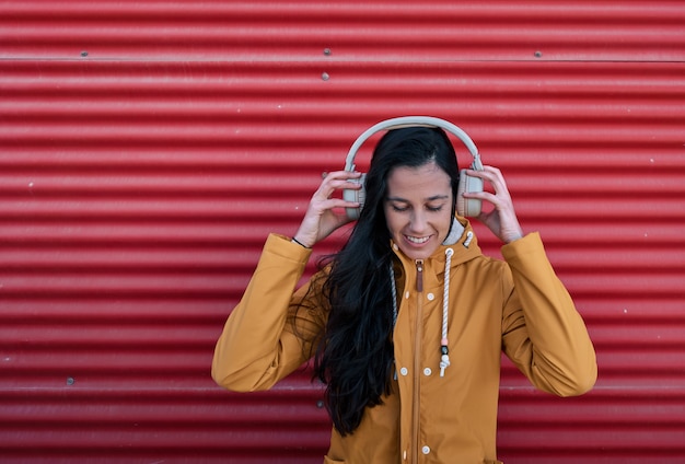 Femme en imperméable jaune, écouter de la musique s'appuyant sur un mur rouge