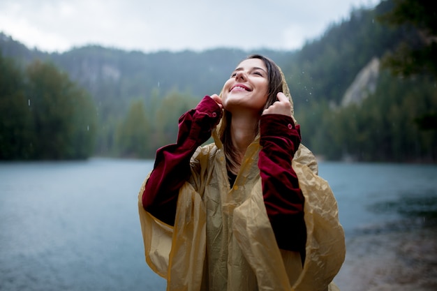 Femme en imperméable près du lac en jour de pluie.