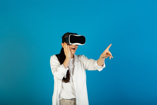 Une femme impressionnée dans des lunettes de réalité virtuelle joue à un jeu vidéo et pointe avec son index