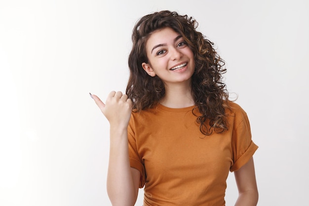 femme inclinant la tête pointant le pouce gauche souriant joyeusement vous demandant de visiter un endroit cool, recommandant un café