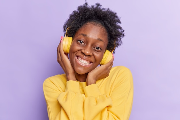 femme incline la tête sourit joyeusement a la bonne humeur tout en écoutant de la musique dans des poses d'écouteurs sur violet