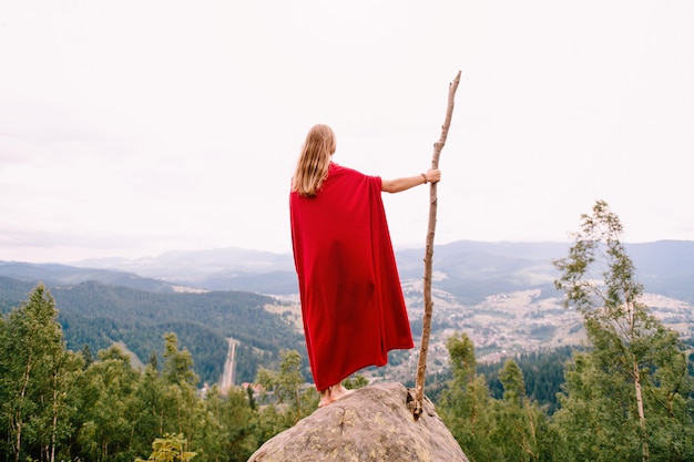 Femme inconnue en cape rouge debout sur la pierre au sommet de la montagne