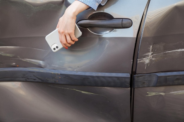 Femme inconnue dans une voiture accidentée, femme sans visage avec la main suspendue à la fenêtre d'une voiture endommagée, personne blessée dans un véhicule brisé. Prise de vue en extérieur.