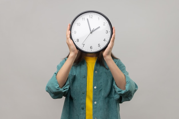 Femme inconnue tenant une horloge murale cachant son calendrier de gestion du temps et rendez-vous de réunion