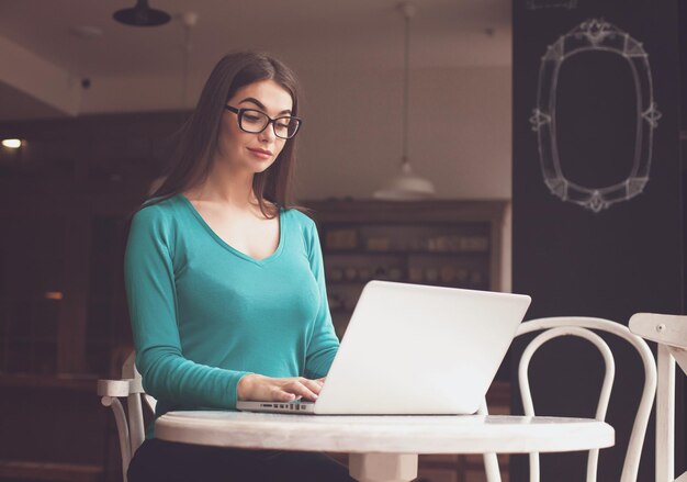 Femme-indépendante avec des lunettes travaille avec son ordinateur portable gris à la table blanche