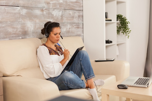 Femme indépendante portant des écouteurs lors d'une vidéoconférence tout en travaillant à domicile.