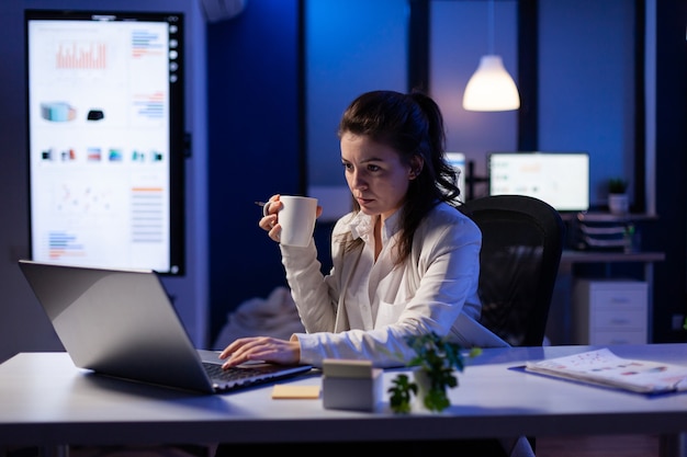 Femme indépendante avec une tasse de café en tapant sur l'ordinateur de l'entreprise