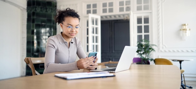 Une femme indépendante travaille dans un espace de coworking de bureau effectue des tâches à l'aide d'un ordinateur portable et d'un téléphone