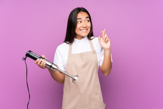 Femme indienne à l'aide d'un mixeur à main isolé sur fond violet avec des doigts traversant