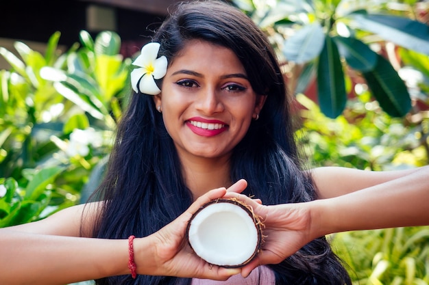 Femme indienne appliquant de l'huile de noix de coco brune foncée cheveux longs dans une main sur le parc d'été vert nature tropicale