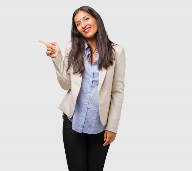 Femme indienne jeune entreprise pointant sur le côté, souriant surpris de présenter quelque chose, naturel et désinvolte