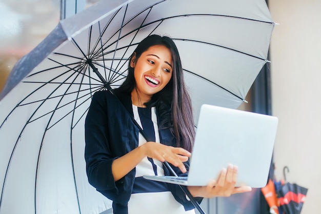 Femme indienne professionnelle avec un grand parapluie tapant sur un ordinateur portable