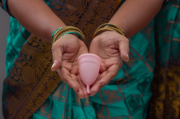 Une femme indienne tenant une coupe menstruelle en silicone réutilisable et montrant différents types de pliage.
