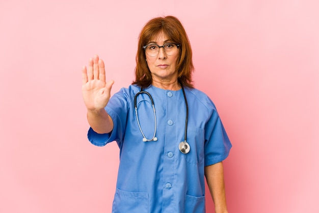 Femme d'infirmière caucasienne d'âge moyen isolée debout avec la main tendue montrant le panneau d'arrêt, vous empêchant.