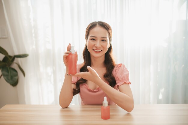 Femme d'influence de beauté heureuse montrant des produits cosmétiques assis à la maison