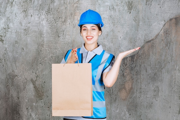 Femme ingénieur en casque bleu et équipement tenant un sac en carton et pointant quelque part