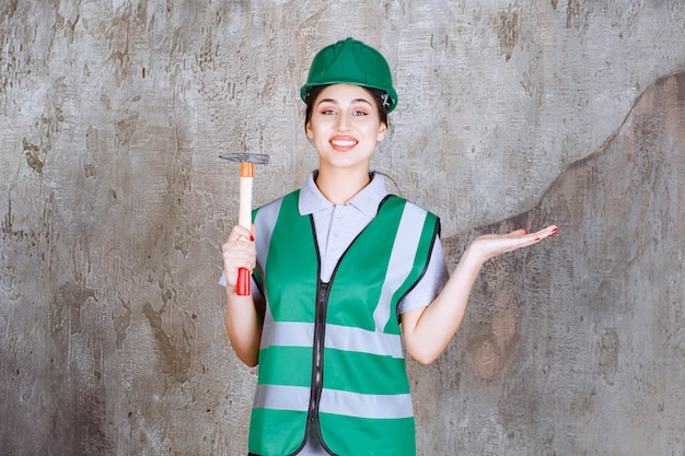 Femme ingénieur en casque vert tenant une hache à manche en bois pour un travail de réparation.