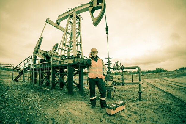 Femme ingénieure dans le champ pétrolifère parlant à la radio portant un casque orange et des vêtements de travail. Contexte du site industriel. Tonifié.